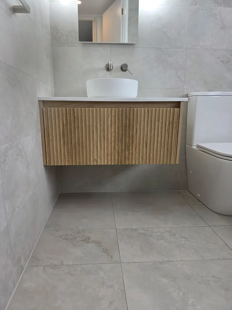 Fluted timber wall hung vanity with a round vessel basin and a wall mounted mixer, over a tiled floor.