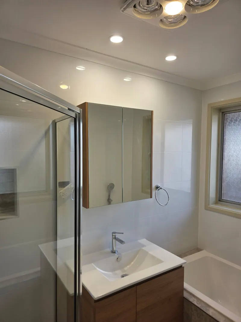 Finished bathroom with a timber framed shaving cabinet over the basin, the shower to one side and the bath beyond.