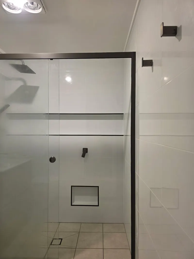 Shower behind a black framed screen, with a rain head and a wall mixer on white tiles.