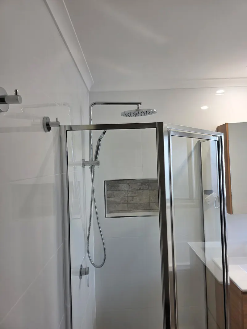 Shower behind a chrome framed screen, with a rain head, a hand shower and a tiled niche.
