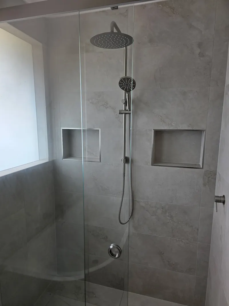 Walk in shower with a rain head, a hand shower and two tiled niches in a grey tiled wall.