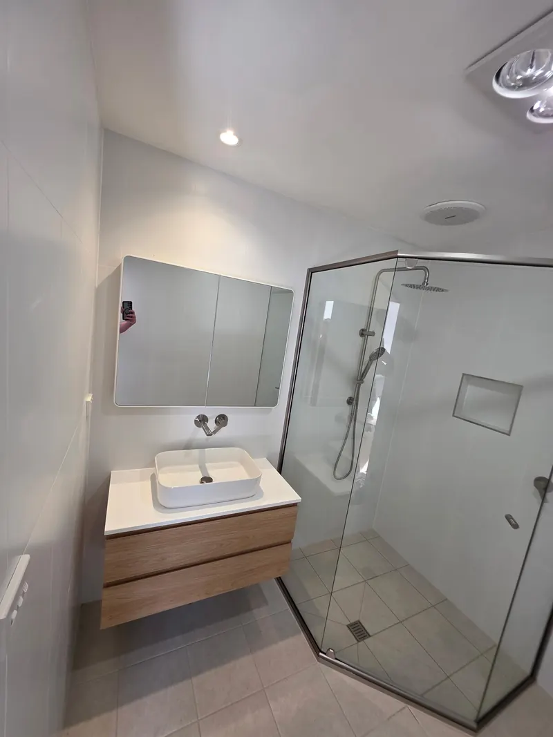 Finished bathroom with a timber wall hung vanity, a vessel basin and a corner shower behind glass.