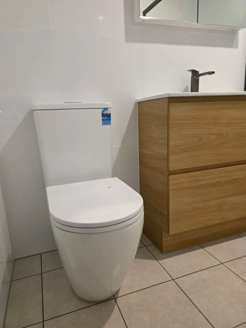 Toilet installed beside a timber vanity with a black mixer, on a tiled bathroom floor.