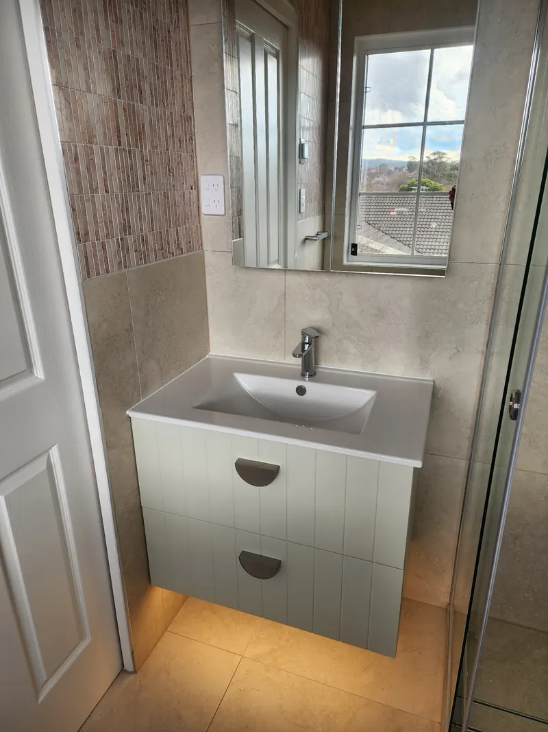 Wall hung vanity under a mirrored cabinet beside a bathroom window, with the shower door alongside.