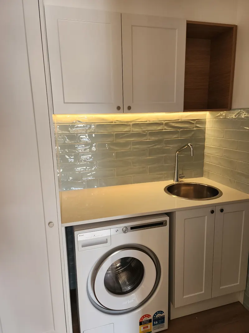 Finished laundry with a stainless tub set into a stone benchtop over a front loading washing machine.